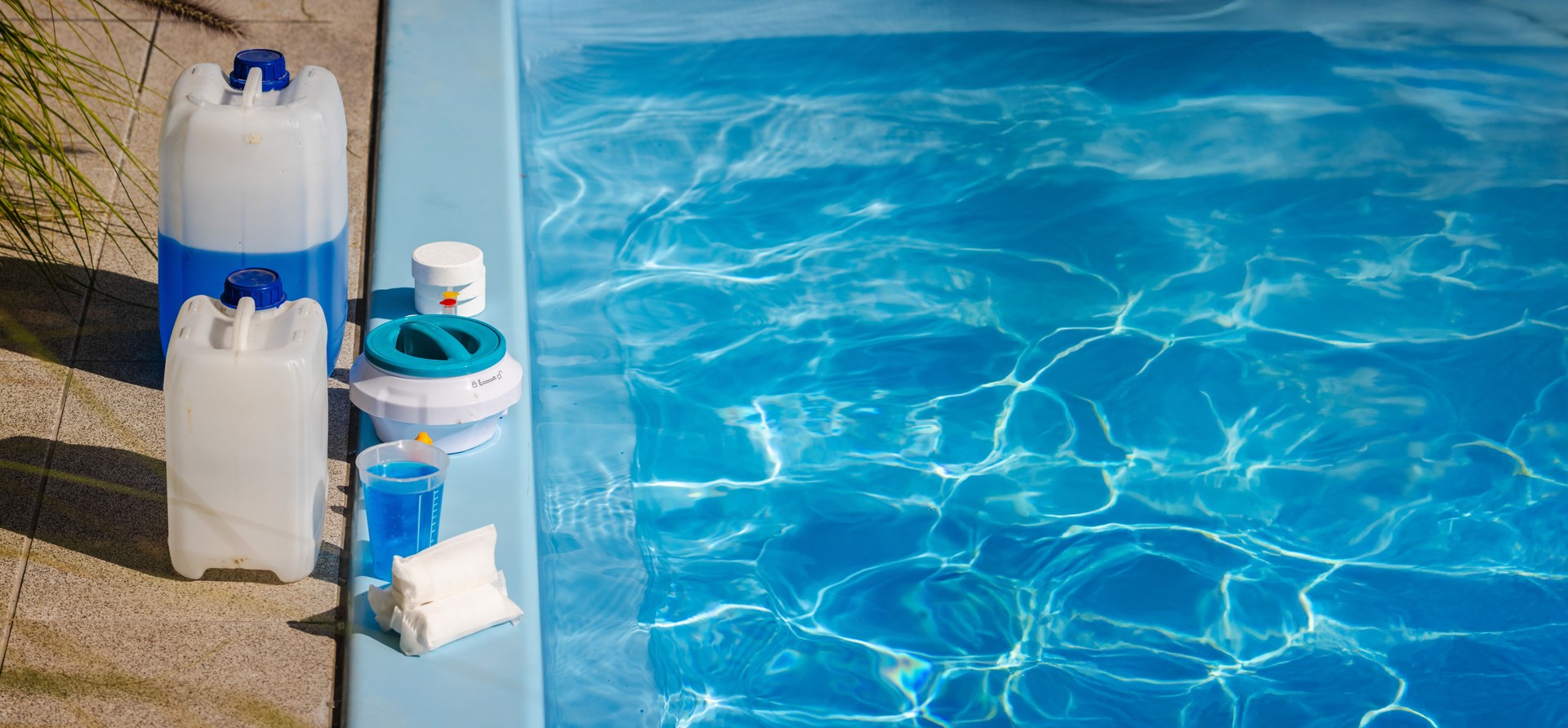 Poolside cleaning kit with blue chemical canisters, chlorine tablets, floating dispenser, measuring cup and sanitizer supplies for swimming pool maintenance